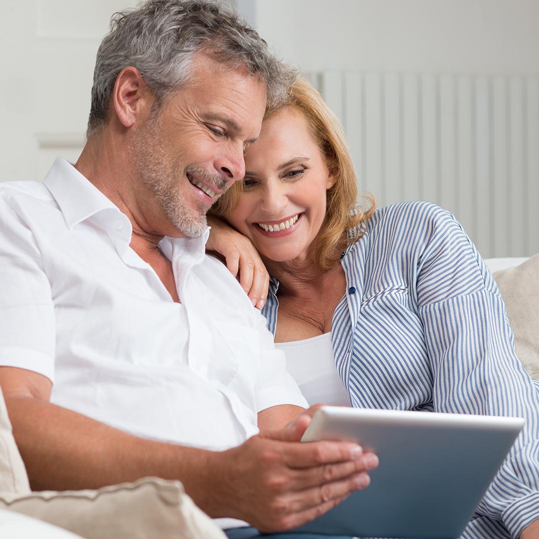 Happy couple sitting on the couch looking at a tablet